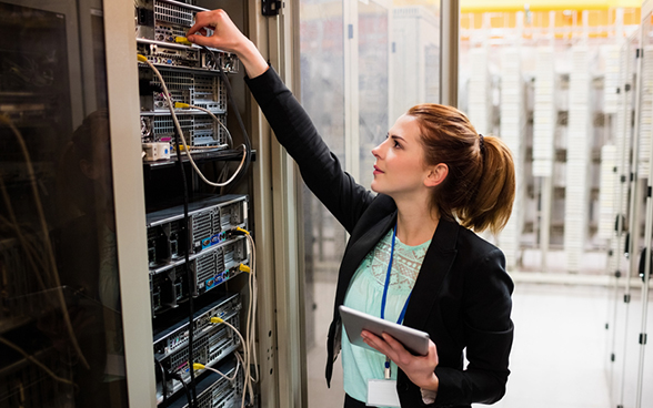 Symbolbild: Eine junge Frau kontrolliert Einstellungen in einem Serverraum